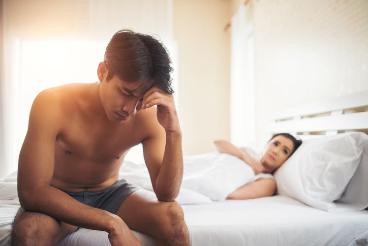 A man feeling sad after sex, sitting on the edge of the bed with his head in his hand, as a woman li...