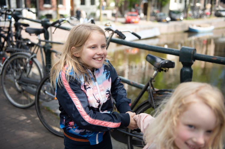 Two Dutch girls in the Netherlands smile as they walk past parked bicycles.