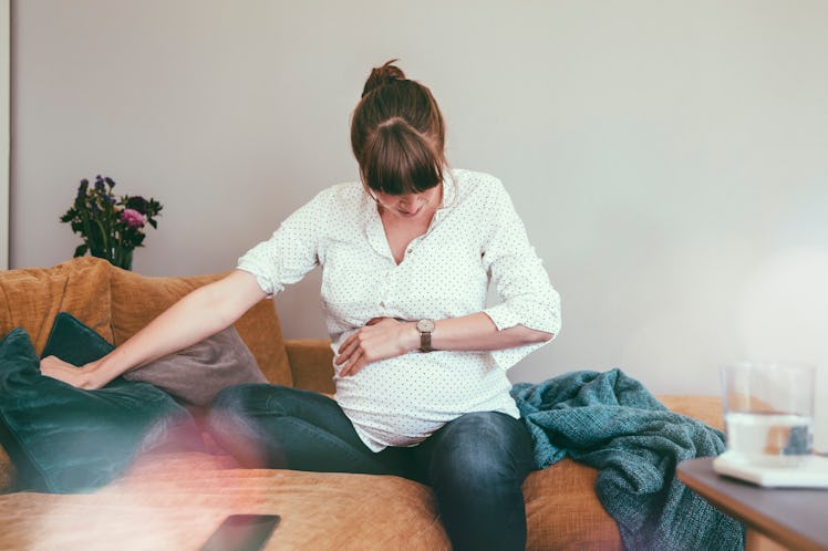 A pregnant woman experiencing the early signs of labor holds her belly bump.