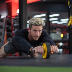 A man doing an ab wheel roller during a love handle workout at the gym.