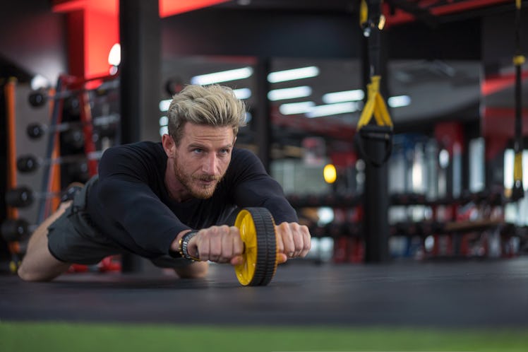 A man doing an ab wheel roller during a love handle workout at the gym.