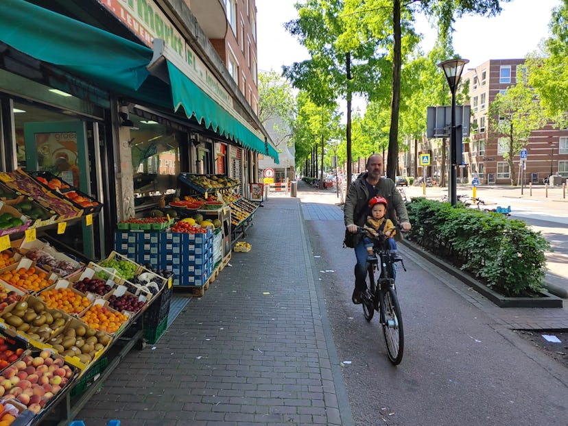 A father and child in the Netherlands cycling past an outdoor grocery market.