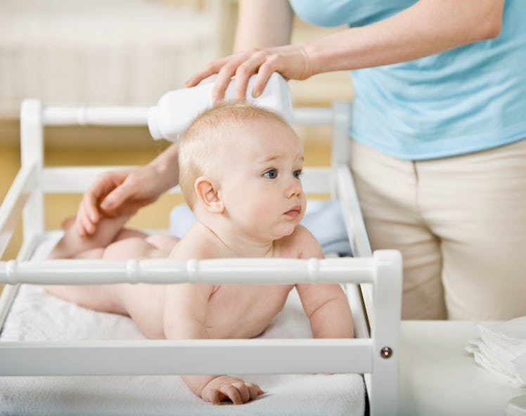A mom applying baby powder to her baby in a crib.