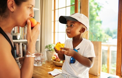 A boy and his mom enjoy a peach in the summer.