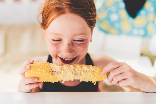 A young redheaded girl eats corn during the summer.
