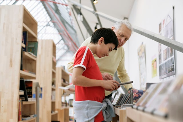A boy looks at CDs at the library with his grandfather.