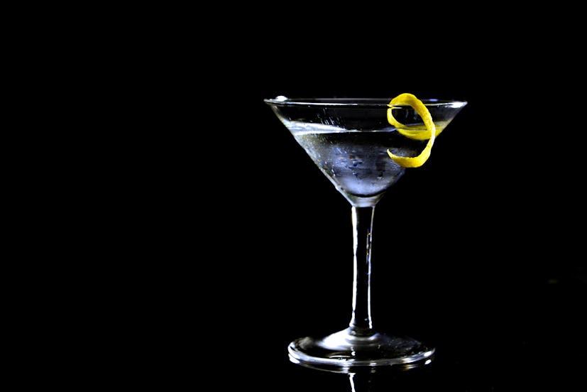 A martini with a twist in a glass before a black background