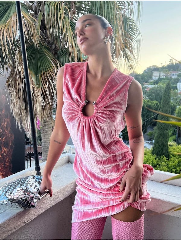Dua Lipa wears a pink velvet dress, boots, and a silver Sardine bag.