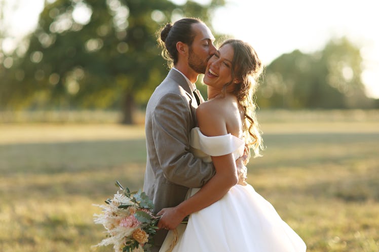 Newlyweds in wedding attire kissing in a field