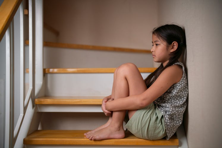 A sad older child sitting alone on the stairs at home.