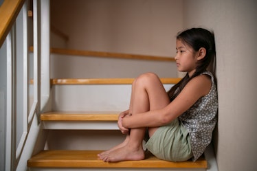 A sad older child sitting alone on the stairs at home.