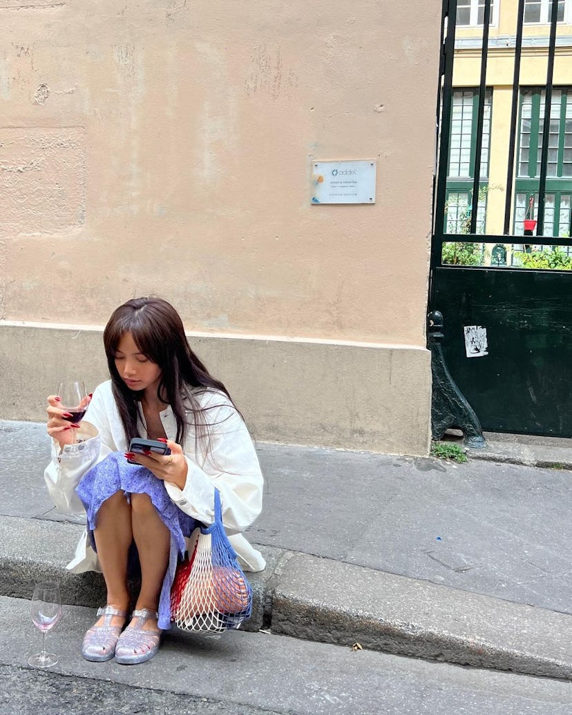 Lisa wears jelly sandals, a reusable shopping bag, white denim jacket, and skirt in a photo posted t...