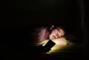 A man awake in bed in the dark, staring at his bright phone.