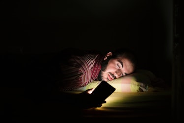 A man awake in bed in the dark, staring at his bright phone.