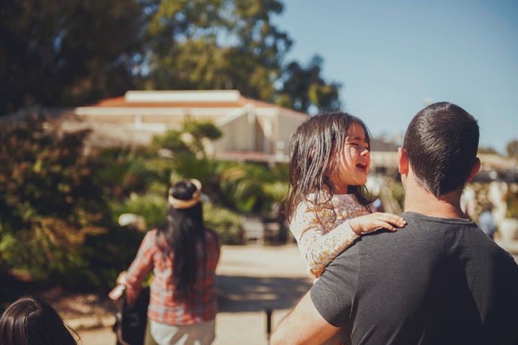 A stubborn child throwing a tantrum while being carried by her dad at a park.