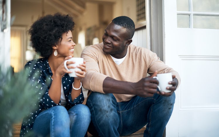 A happy couple drinking from mugs while sitting together.