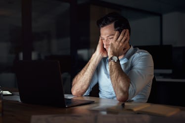 A tired man working on his laptop on no sleep.