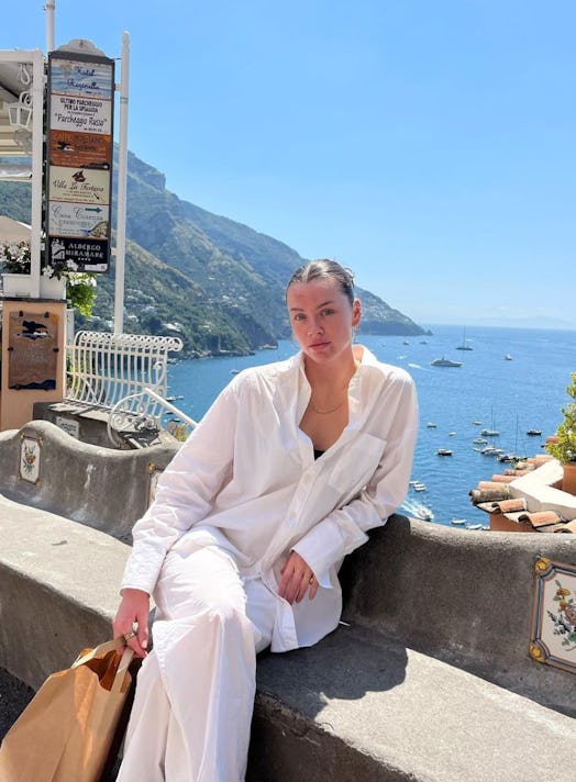 woman in white linen set sits on on bench with beautiful sunny scenery behind her