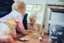 一个baby crawling on the floor, looking in the mirror.