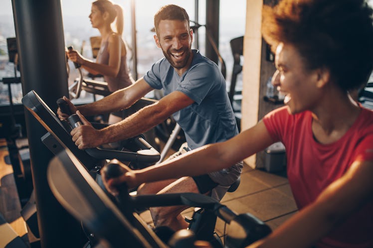 A man and woman in a cycling workout class laughing together.