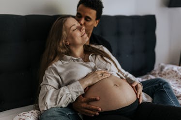 A man holding and kissing a pregnant woman in bed.