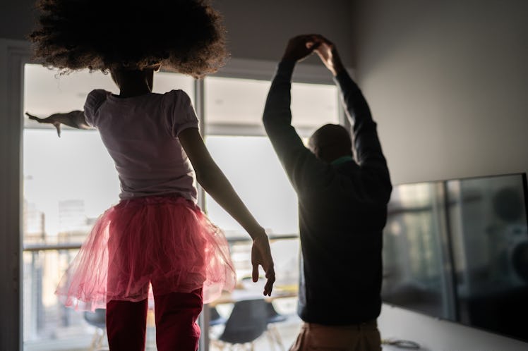 A dad and his daughter, who is wearing a pink tutu, dancing together at home.