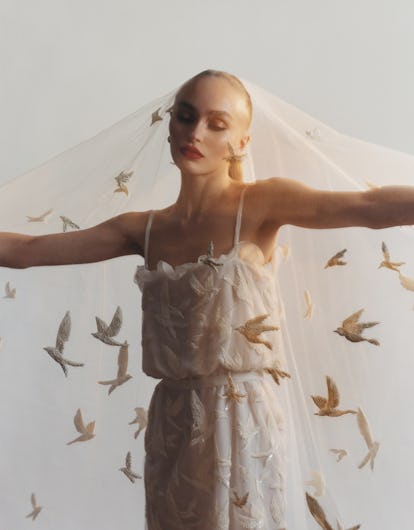 the model and actress Lily-Rose Depp wearing a while Chanel dress and veil. Her arms are outstretche...