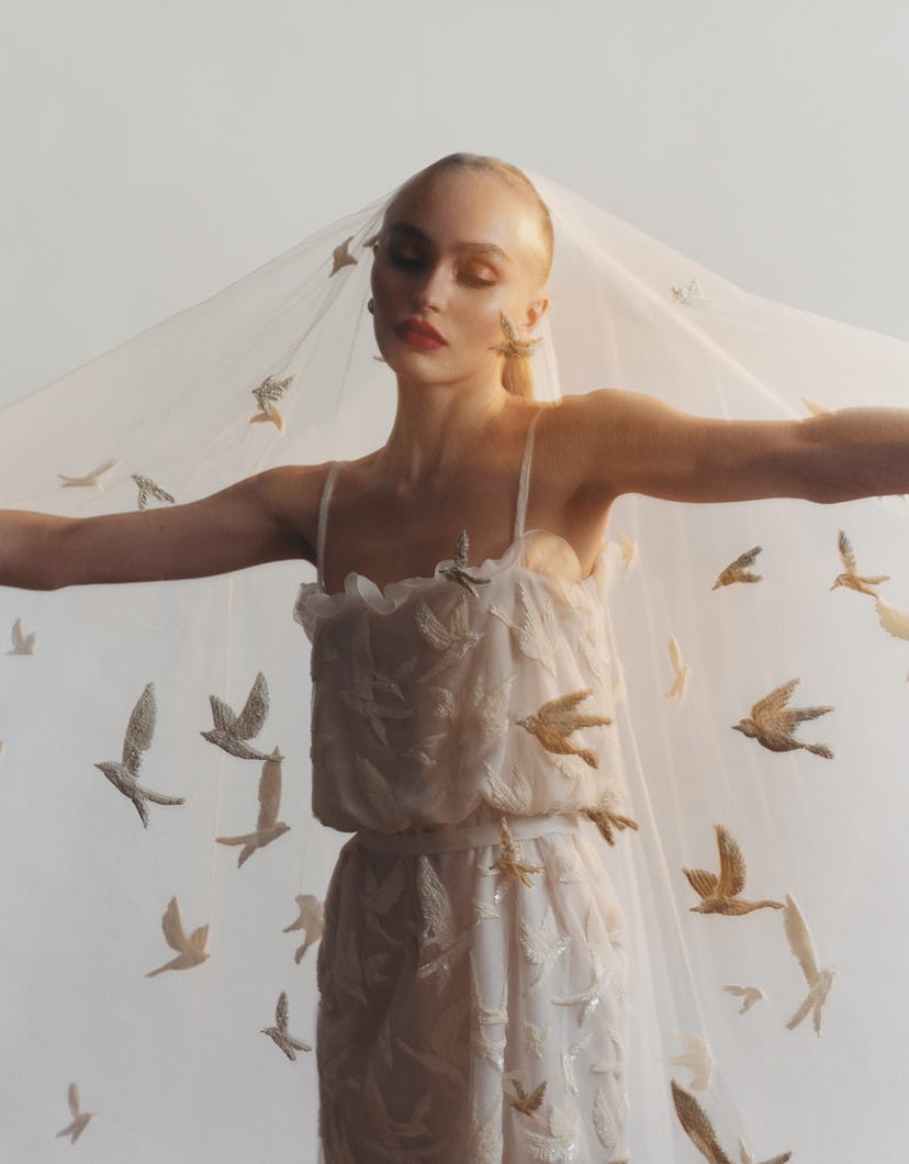 the model and actress Lily-Rose Depp wearing a while Chanel dress and veil. Her arms are outstretche...