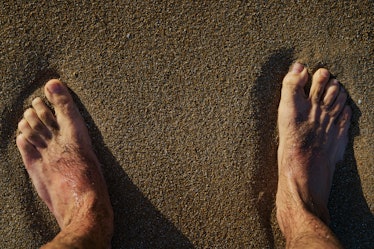 Close up of a man's hairy feet and hairy toes standing on sand.
