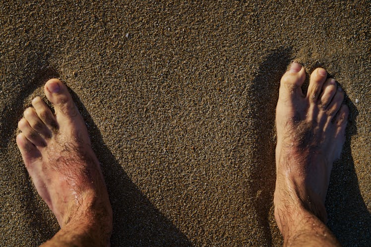 Close up of a man's hairy feet and hairy toes standing on sand.