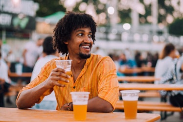 A man outdoors drinking beer, with two more beers on the table.