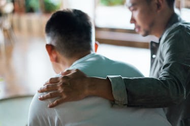 A man comforting another man, with an arm around his shoulders.