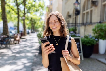 Woman in black dress looking at text message on phone and smiling happily