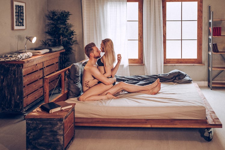 Woman in underwear sitting on man's lap in bed as they look into one another's eyes