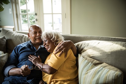 Elderly couple smiling and hugging on a couch 
