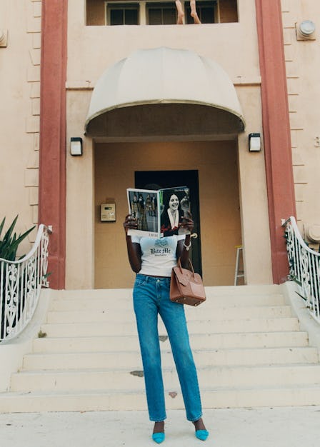 a model standing on a stoop holding a magazine in front of her face, with an hermes bag held in the ...