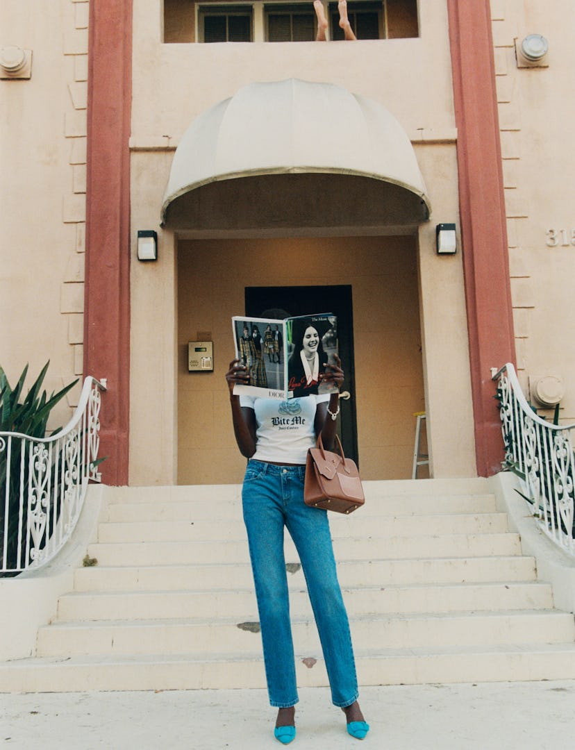 a model standing on a stoop holding a magazine in front of her face, with an hermes bag held in the ...