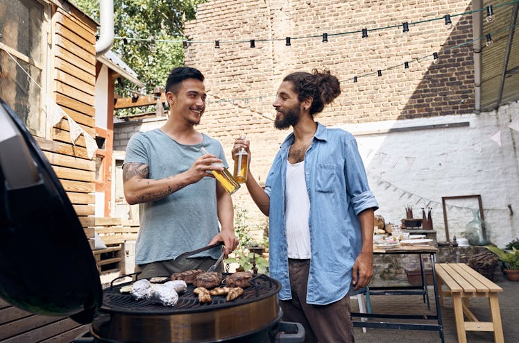 Two men drinking beer at a cookout while grilling meat.