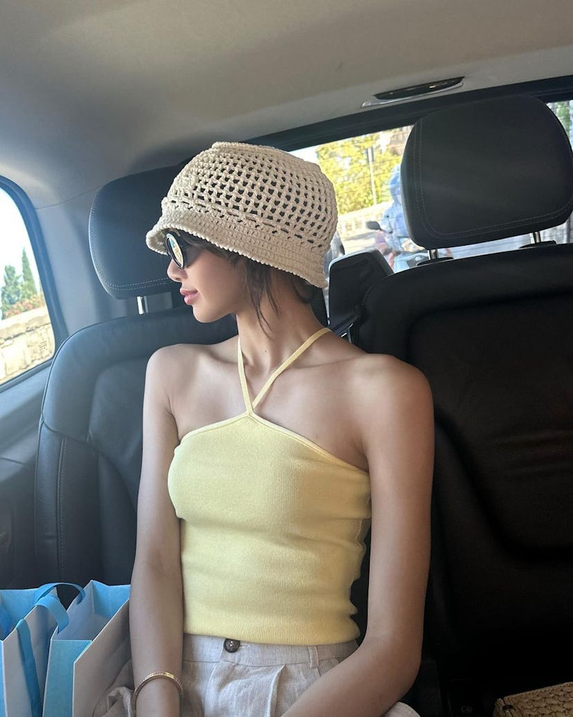 Lisa of Blackpink wears a yellow tank top, linen pants, and a crochet bucket hat in a photo posted t...