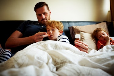 A dad in bed with his two kids, sick with COVID, giving one of them medicine.
