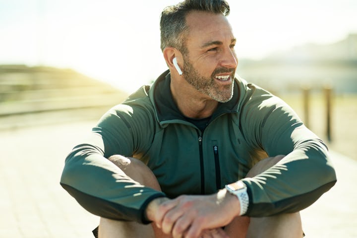 A man practicing good mental health habits sitting outdoors, smiling, with headphones in.