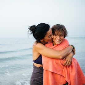 A woman hugs her son on the beach.