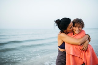 A woman hugs her son on the beach.