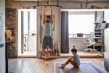 A man does a chin up bodyweight back exercise at home while his son sits with him.