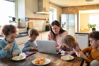 A mom looks over her budget while eating breakfast with her kids.