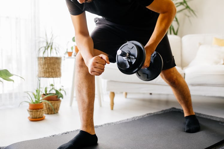 A man in a black shirt and shorts doing a dumbbell workout at home for building muscle