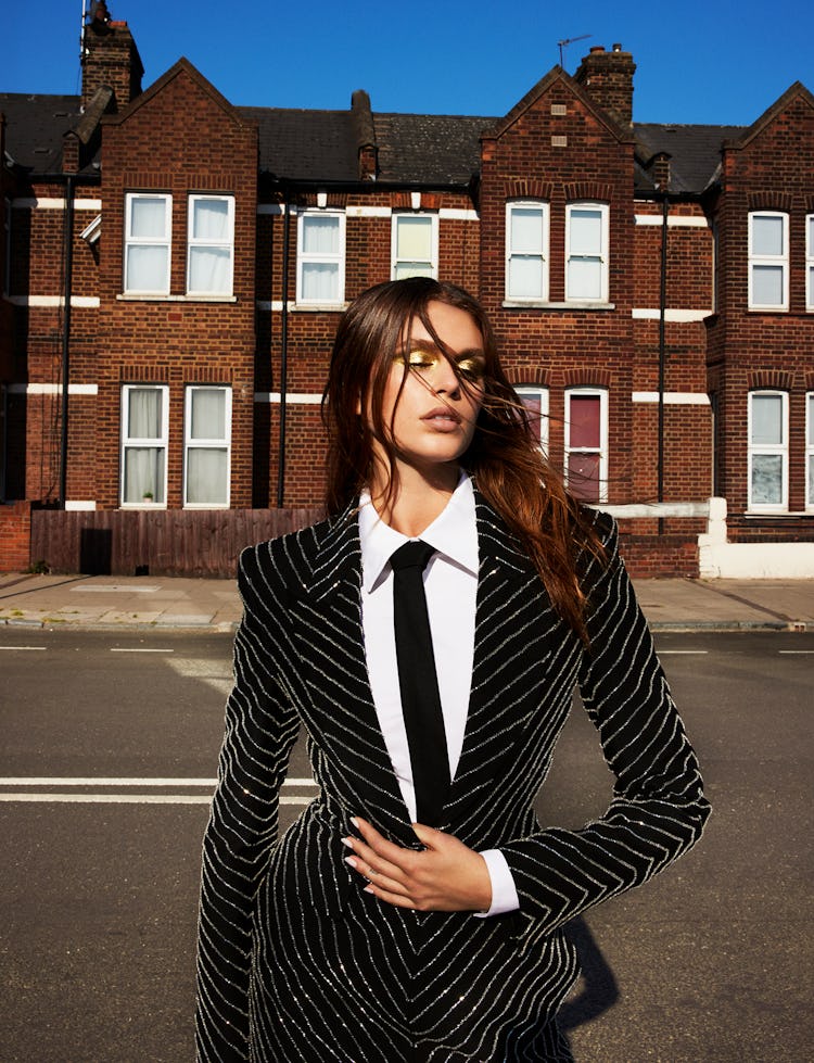 Model Kaia Gerber wears a  black pinstripe glitter blazer, white button down shirt and black tie.