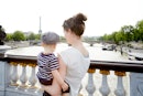 A mom and baby in France, standing on a bridge overlooking the Eiffel Tower.
