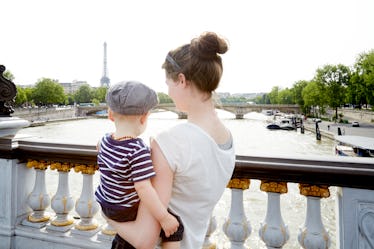 A mom and baby in France, standing on a bridge overlooking the Eiffel Tower.