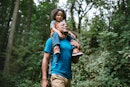 A dad with his child on his shoulders goes on a walk in a forest for his mental health.